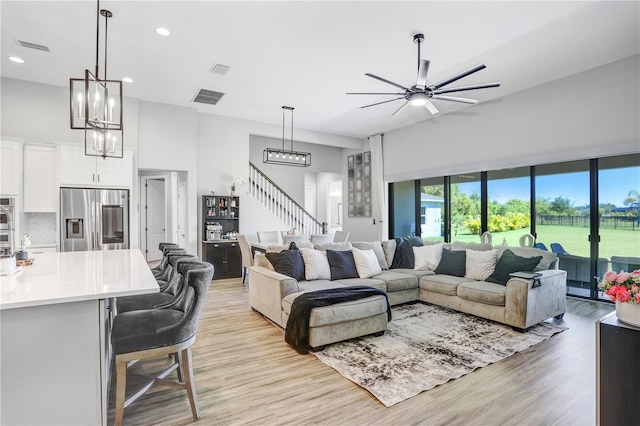 living room with a high ceiling, ceiling fan with notable chandelier, and light hardwood / wood-style flooring