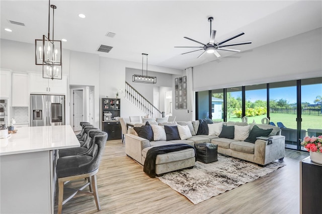 living room featuring a towering ceiling, light wood-type flooring, and ceiling fan with notable chandelier