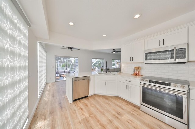 kitchen featuring white cabinetry, light wood-type flooring, stainless steel appliances, kitchen peninsula, and ceiling fan