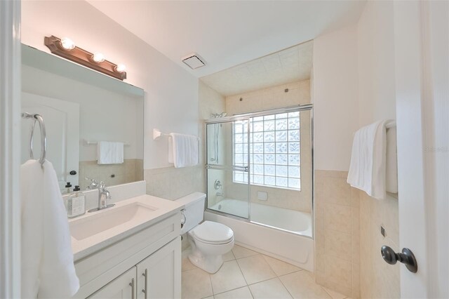 full bathroom with tile flooring, oversized vanity, toilet, and bath / shower combo with glass door