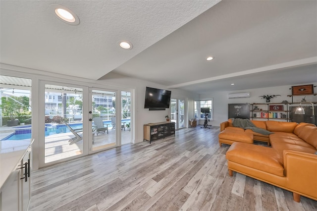 living room featuring light hardwood / wood-style floors, a textured ceiling, and a wall mounted air conditioner