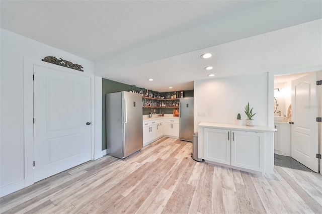 kitchen featuring white cabinets, stainless steel fridge, light hardwood / wood-style flooring, and kitchen peninsula