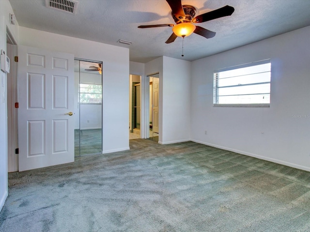 unfurnished bedroom with multiple windows, a textured ceiling, carpet flooring, and ceiling fan