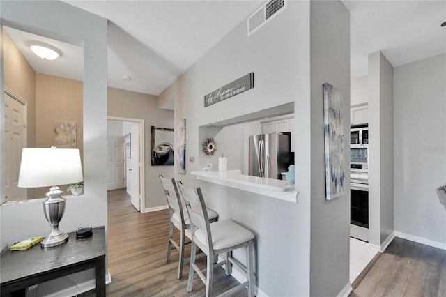 kitchen featuring stainless steel appliances, a kitchen bar, light hardwood / wood-style flooring, and white cabinets