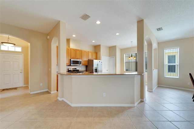 kitchen with appliances with stainless steel finishes, a kitchen island, light tile floors, and pendant lighting