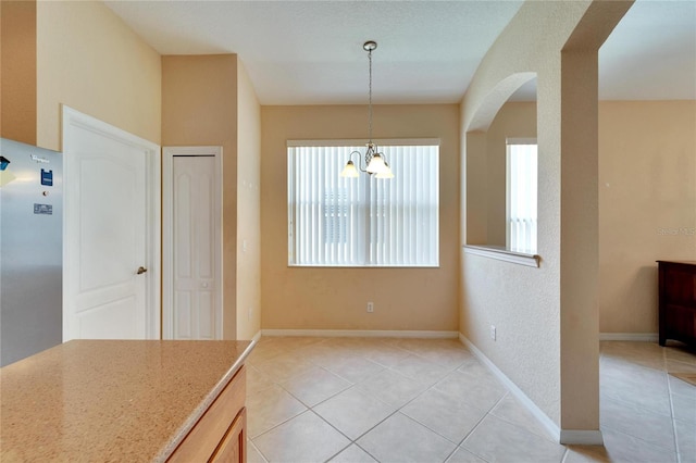 kitchen featuring stainless steel refrigerator, light stone countertops, light tile floors, and pendant lighting