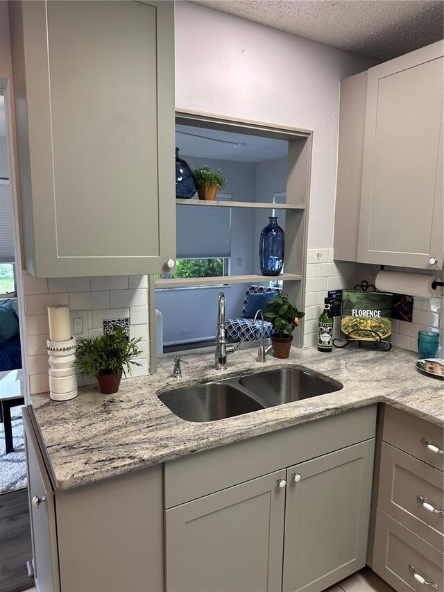 kitchen featuring wood-type flooring, light stone counters, a textured ceiling, tasteful backsplash, and sink