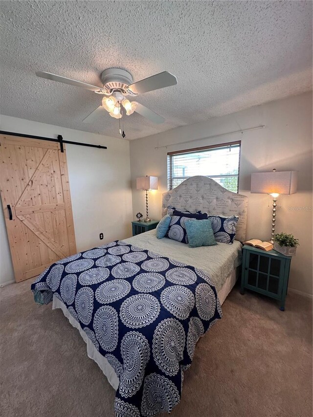 bedroom with ceiling fan, a textured ceiling, a barn door, and carpet