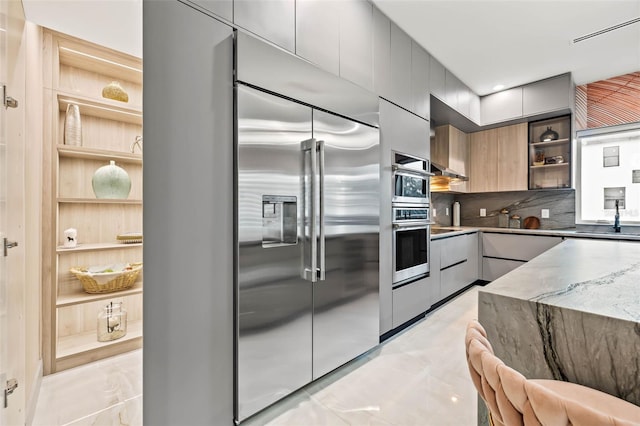 kitchen featuring stainless steel appliances, sink, decorative backsplash, stone countertops, and gray cabinetry