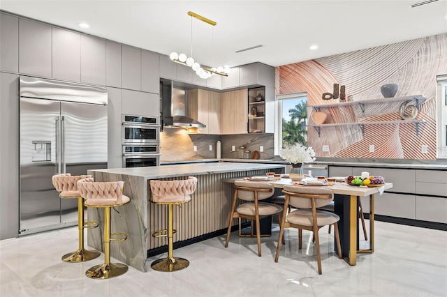 kitchen featuring stainless steel appliances, decorative backsplash, gray cabinetry, and wall chimney exhaust hood