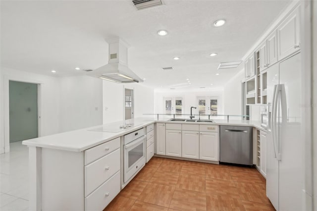 kitchen featuring white appliances, white cabinets, a peninsula, light countertops, and a sink