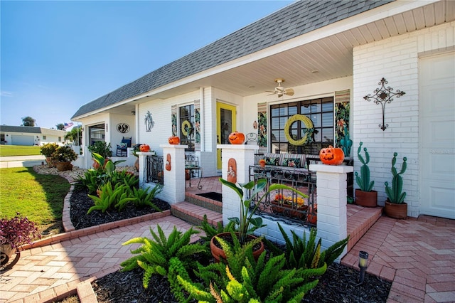 entrance to property featuring brick siding, a shingled roof, covered porch, ceiling fan, and a garage