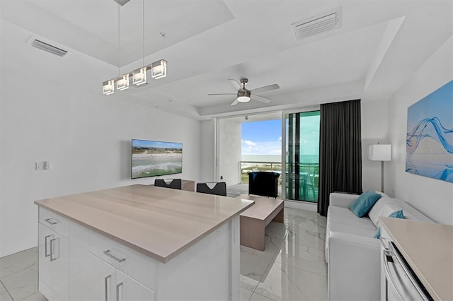 kitchen featuring ceiling fan, a raised ceiling, a center island, white cabinets, and light tile floors