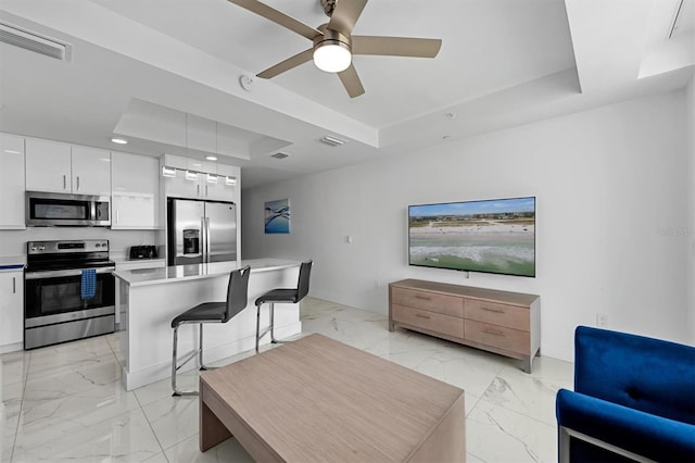 living room with ceiling fan, a tray ceiling, and light tile floors