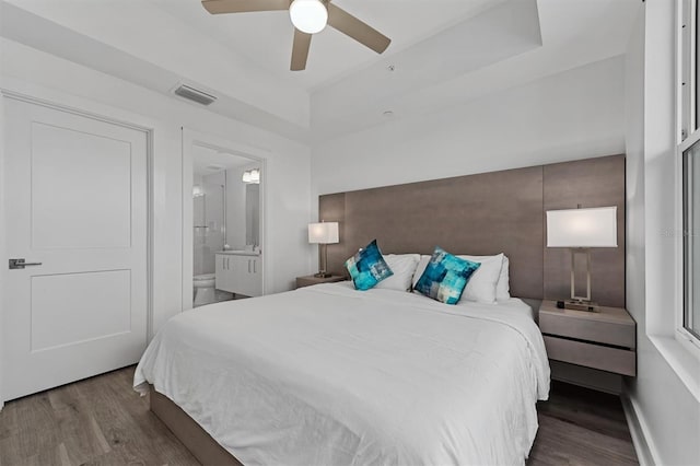 bedroom with connected bathroom, dark hardwood / wood-style flooring, ceiling fan, and a raised ceiling