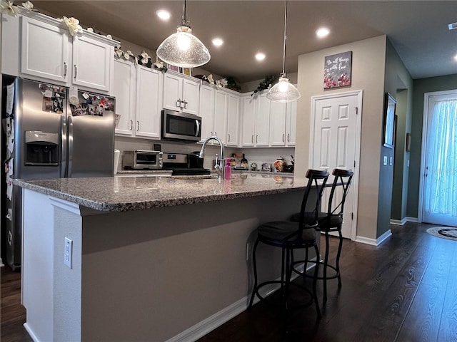 kitchen featuring stainless steel appliances, a center island with sink, white cabinetry, dark wood-type flooring, and pendant lighting