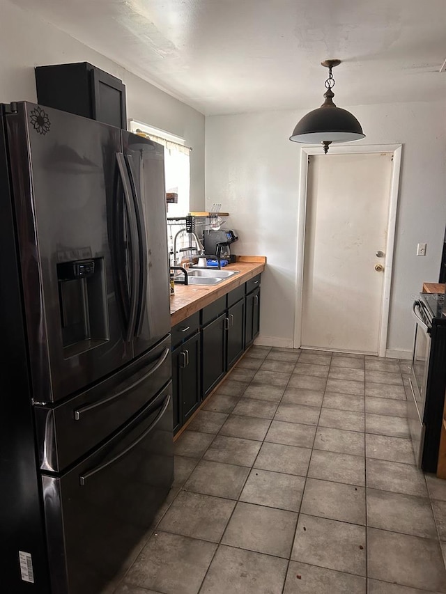 kitchen with stainless steel range with electric cooktop, decorative light fixtures, black fridge, tile floors, and sink