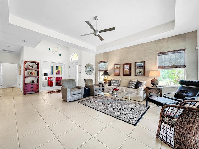 living room with ceiling fan, light tile floors, and a raised ceiling