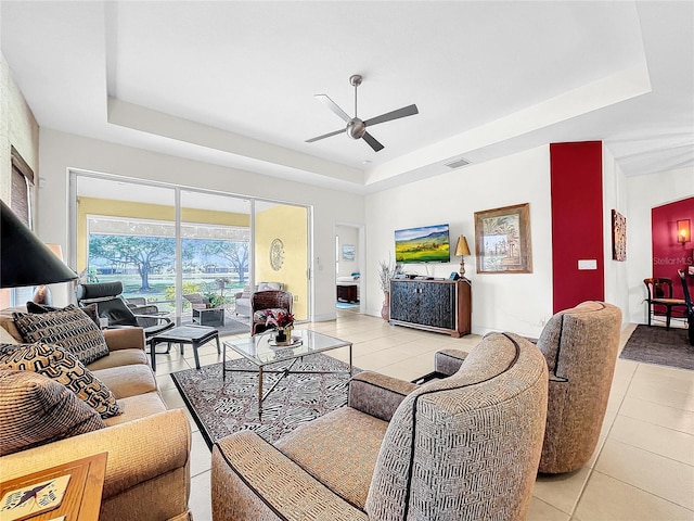 living room with a tray ceiling, ceiling fan, and tile floors