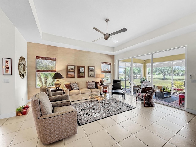 tiled living room with ceiling fan and a raised ceiling