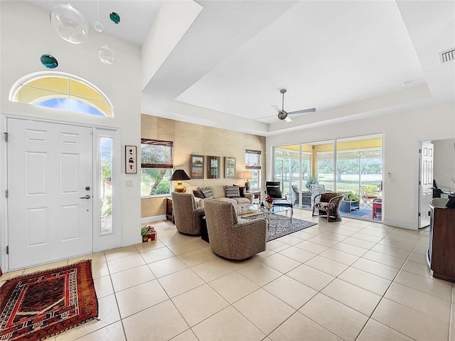 living room with ceiling fan, a tray ceiling, and light tile floors