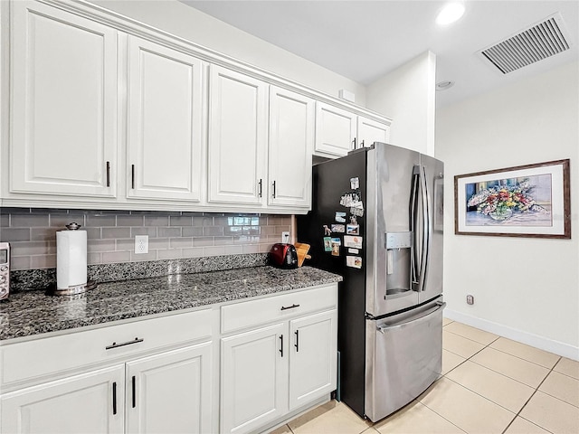 kitchen with light tile flooring, dark stone countertops, backsplash, stainless steel fridge with ice dispenser, and white cabinetry