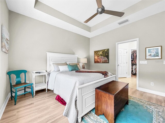 bedroom with light hardwood / wood-style floors, a walk in closet, a closet, and ceiling fan