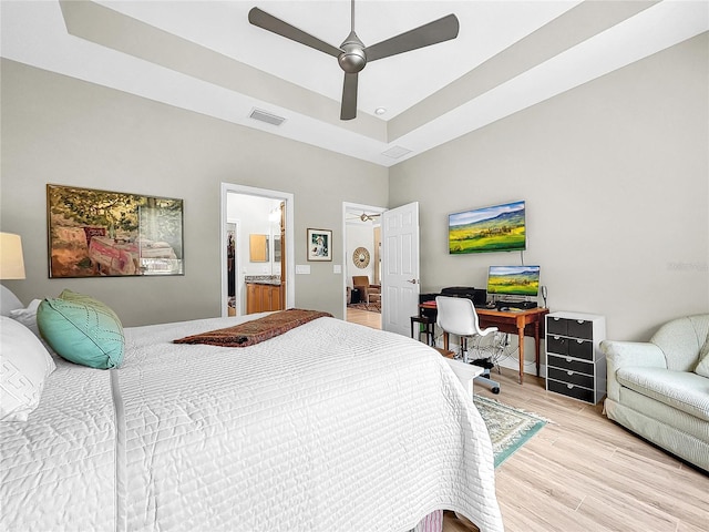 bedroom featuring light hardwood / wood-style floors, ceiling fan, connected bathroom, and a raised ceiling