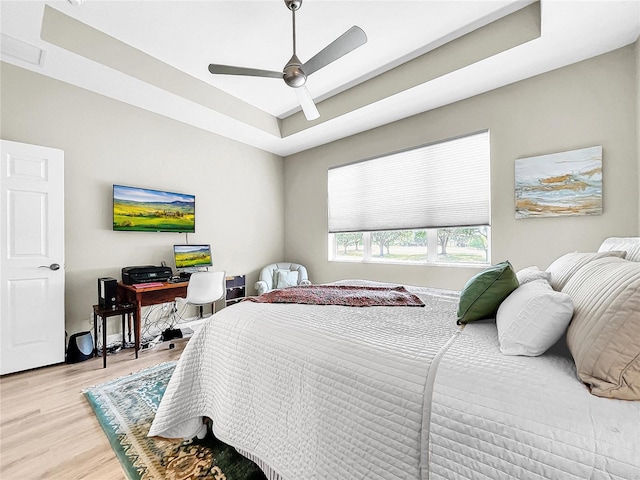 bedroom with ceiling fan, light hardwood / wood-style floors, and a raised ceiling