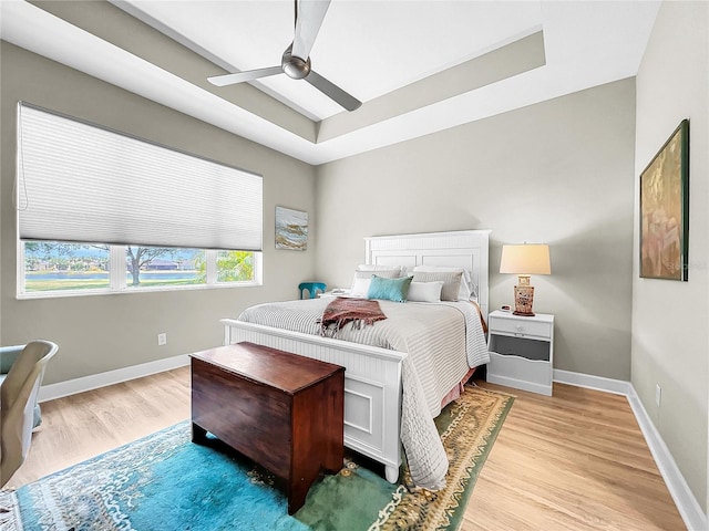 bedroom featuring a raised ceiling, ceiling fan, and light wood-type flooring