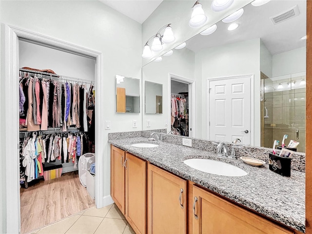 bathroom with dual sinks, a shower with shower door, large vanity, and wood-type flooring