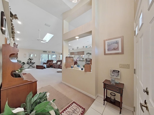 foyer entrance featuring a towering ceiling, ceiling fan, light tile flooring, and a skylight