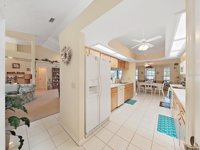 kitchen with light brown cabinets, ceiling fan, a raised ceiling, light colored carpet, and white appliances