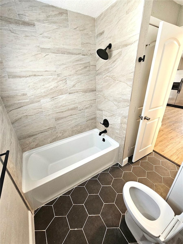 bathroom featuring tiled shower / bath, tile flooring, and toilet