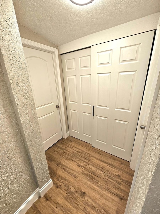 hallway featuring a textured ceiling, dark wood-type flooring, and lofted ceiling