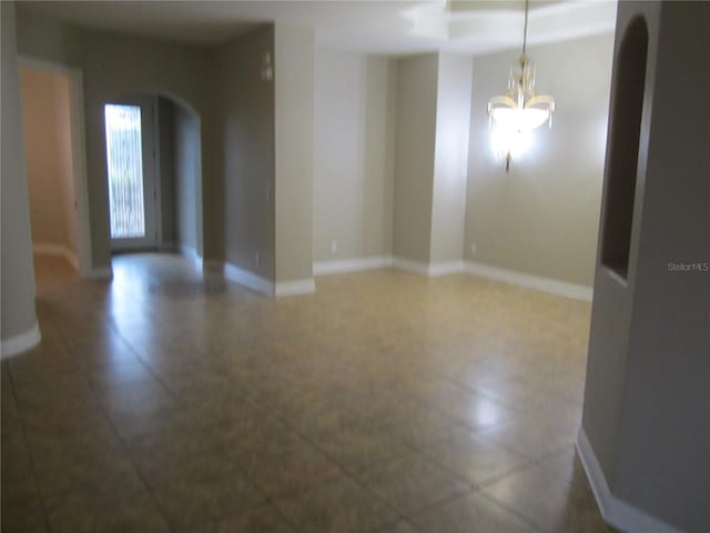 empty room featuring dark tile flooring and an inviting chandelier