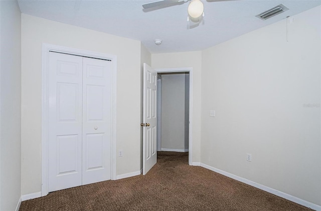 unfurnished bedroom with ceiling fan, a closet, and dark colored carpet