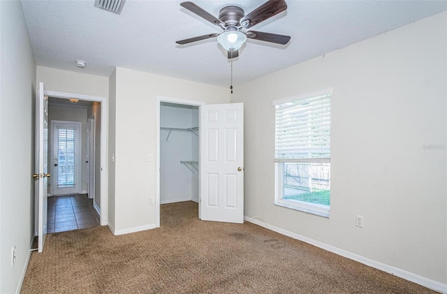 unfurnished bedroom with carpet, a spacious closet, ceiling fan, and multiple windows