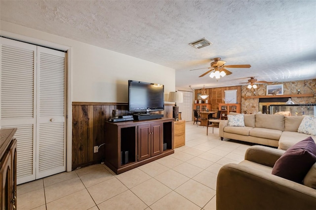 living room featuring a textured ceiling, light tile patterned flooring, wooden walls, and ceiling fan