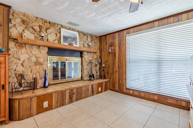 interior space featuring a textured ceiling, light tile patterned flooring, wood walls, and ceiling fan