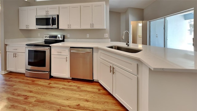 kitchen featuring light wood-type flooring, stainless steel appliances, white cabinets, kitchen peninsula, and sink