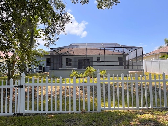 rear view of house featuring glass enclosure and a lawn