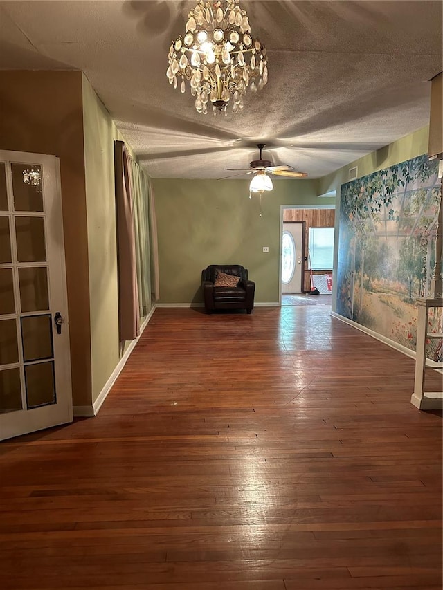 unfurnished living room with ceiling fan with notable chandelier, dark hardwood / wood-style flooring, and a textured ceiling