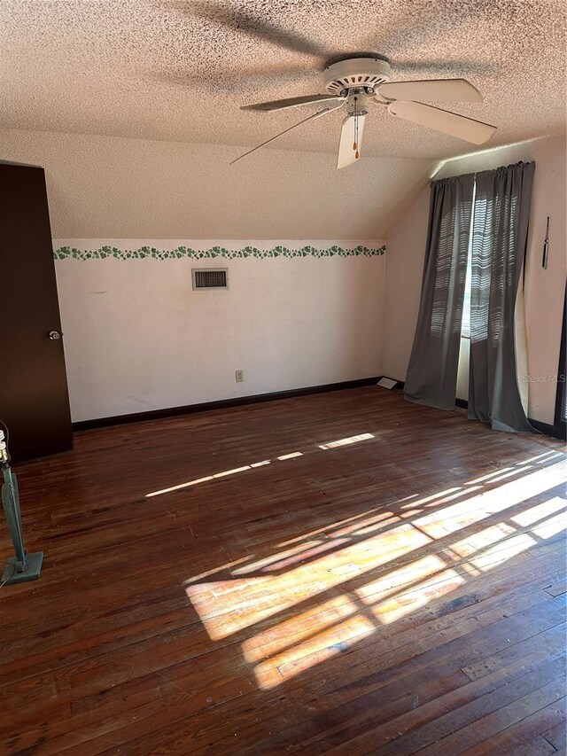 empty room featuring a textured ceiling, dark hardwood / wood-style floors, and lofted ceiling