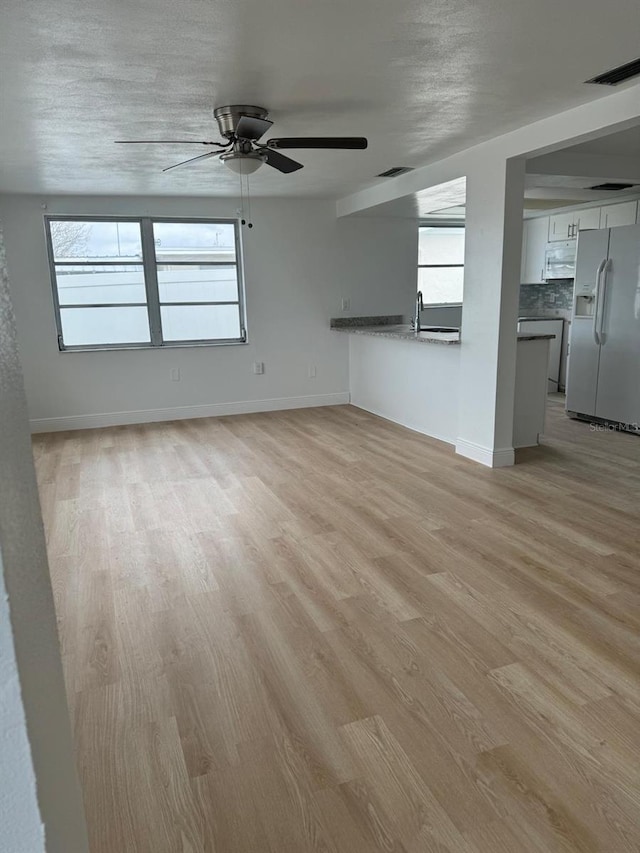 unfurnished living room featuring ceiling fan, a textured ceiling, a wealth of natural light, and light hardwood / wood-style flooring