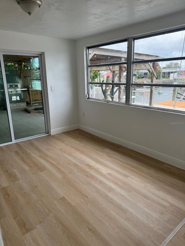 spare room featuring a water view, a textured ceiling, and light wood-type flooring