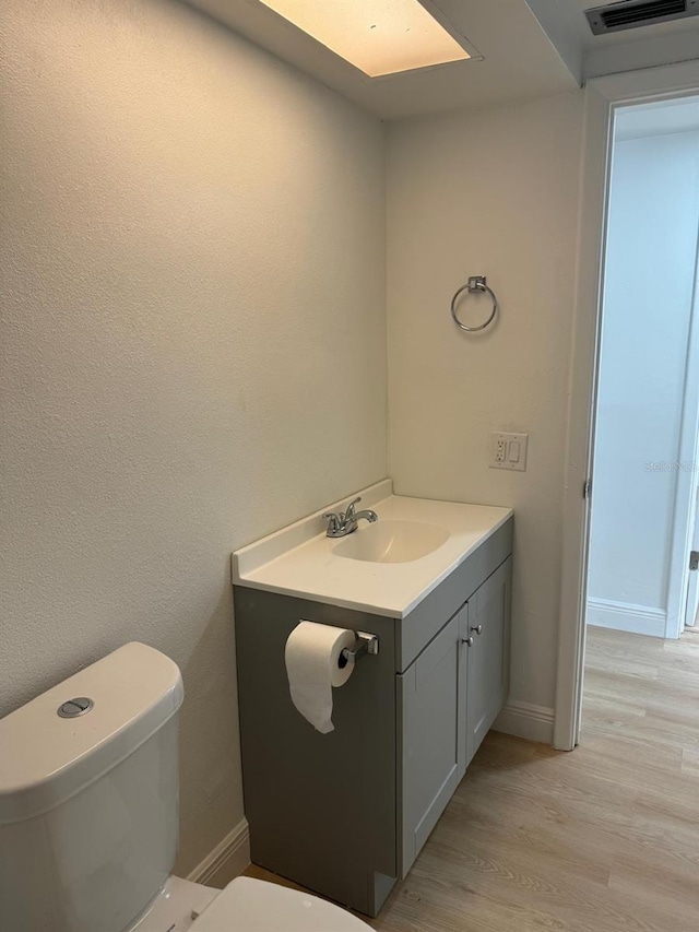 bathroom with a skylight, hardwood / wood-style floors, vanity, and toilet