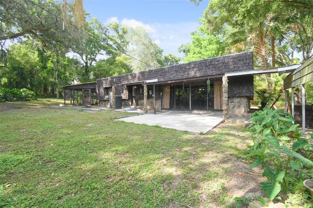 rear view of property with stone siding, mansard roof, a lawn, a patio area, and a shingled roof