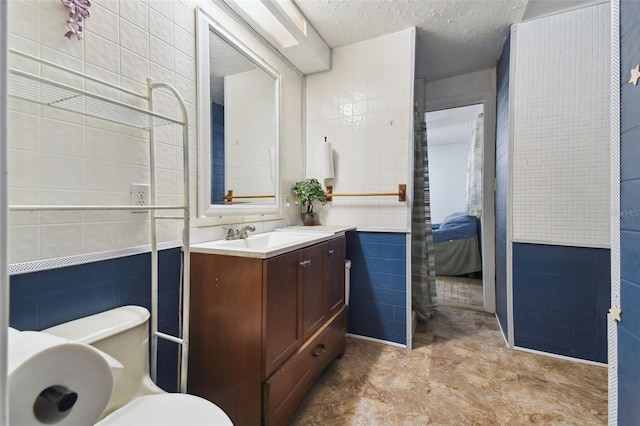 bathroom with connected bathroom, toilet, tile walls, a textured ceiling, and vanity