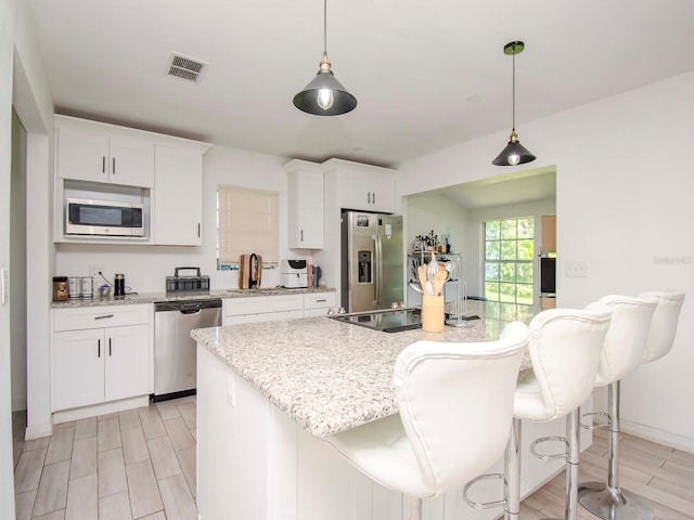 kitchen with a kitchen island, a kitchen breakfast bar, hanging light fixtures, white cabinets, and appliances with stainless steel finishes